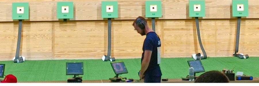 Bosnian sport shooter Boris Filipovac standing alone on the shooting line, seemingly deep in thought, perhaps battling performance pressure, with a line of targets in the background.