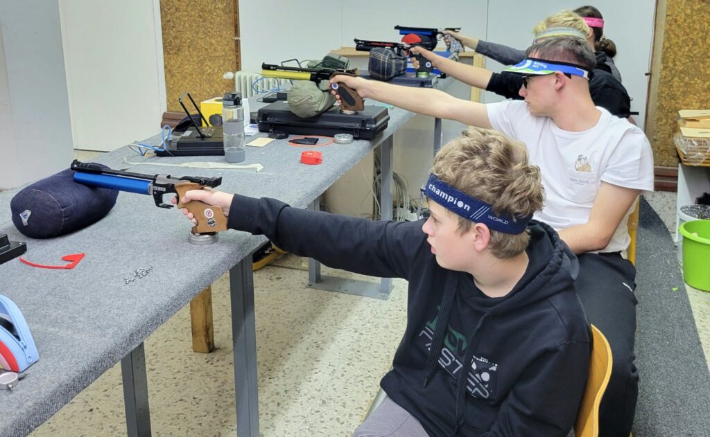 Fixing one of the most common shooting mistakes, several young pistol shooters sit on the firing line with their pistols supported and work on their triggering.