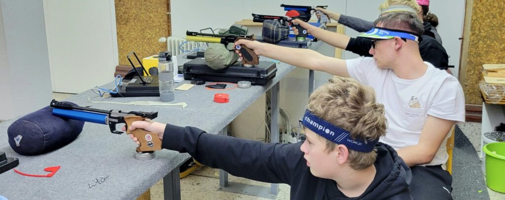 Fixing one of the most common shooting mistakes, several young pistol shooters sit on the firing line with their pistols supported and work on their triggering.